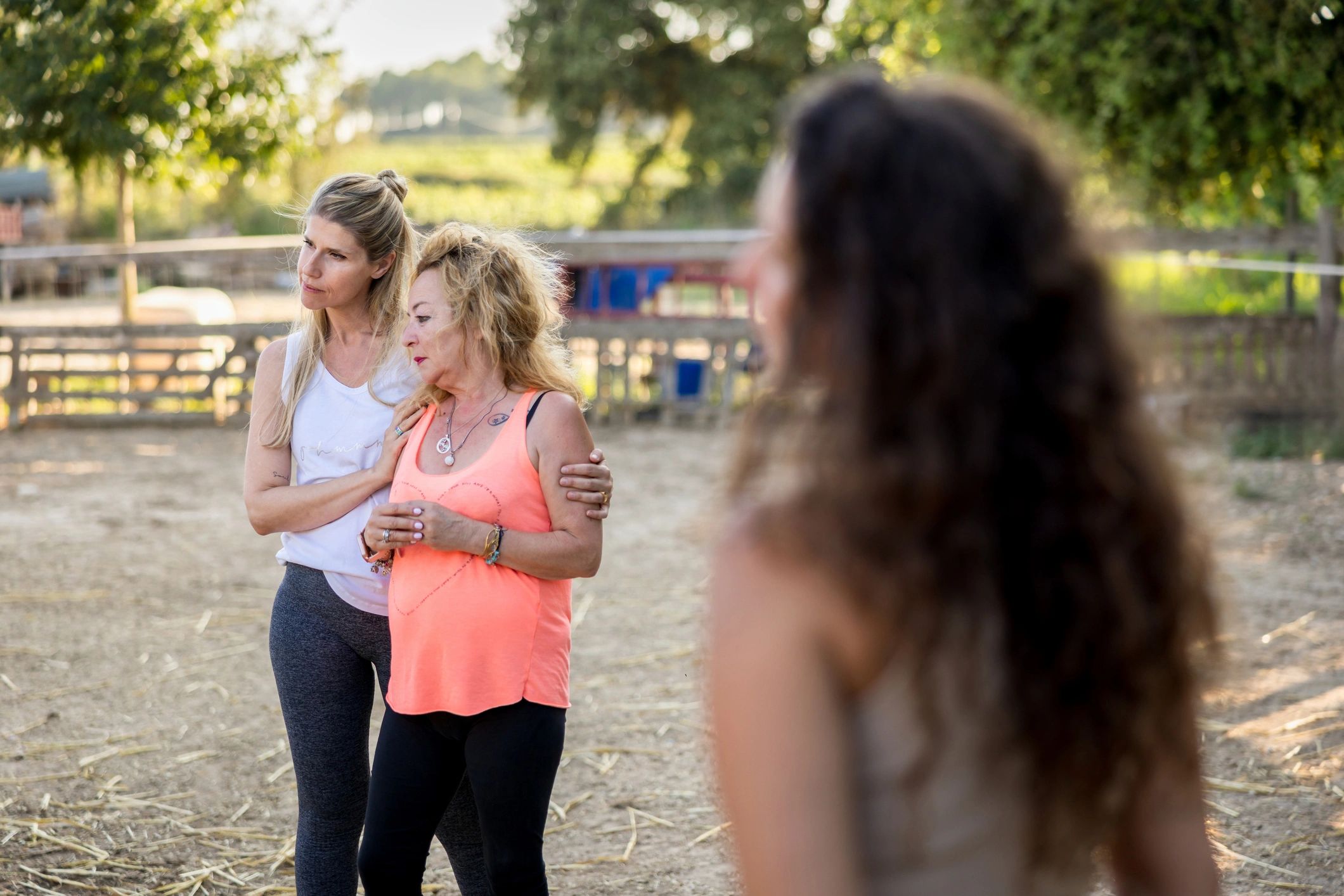 Women supporting each other during equine-assisted therapy, sharing emotional healing moments near horses in tranquil outdoor environment